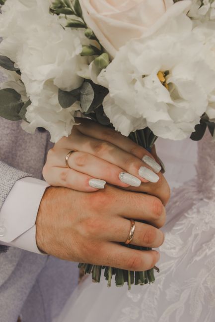 Close-up of a couple holding a bouquet of fresh wedding flowers, featuring white lisianthus and eustoma with hints of greenery, wrapped in elegant white paper and tied with a silver ribbon. The bride'